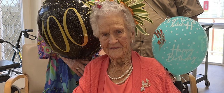 Lady in pink smiles at the camera with birthday balloons in the background 